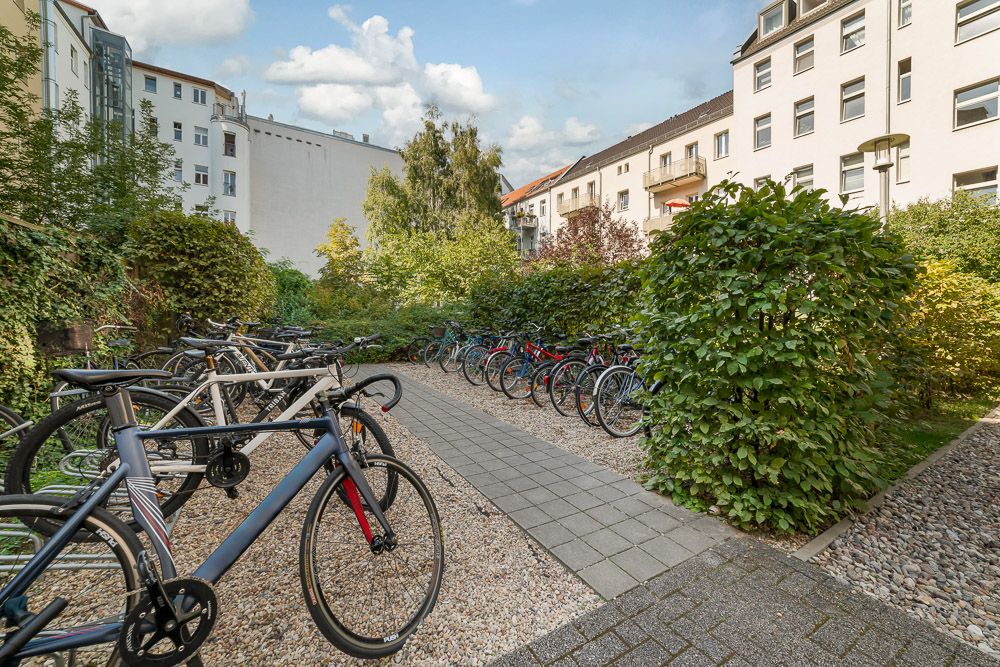 Fahrradstellplätze im begrünten Innenhof eines Wohngebäudes, umgeben von Hecken und Bäumen.