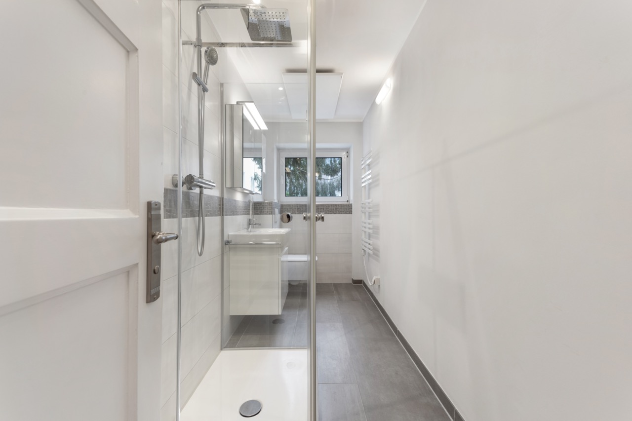 Modernes, schmales Badezimmer mit Dusche, Waschbecken, Toilette und Fenster.