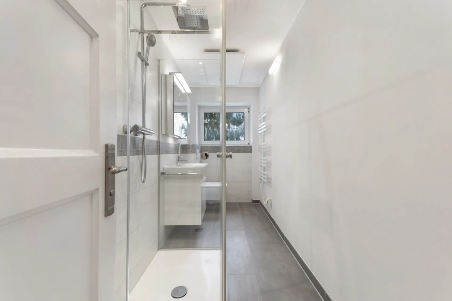 Modernes, schmales Badezimmer mit Dusche, Waschbecken, Toilette und Fenster.