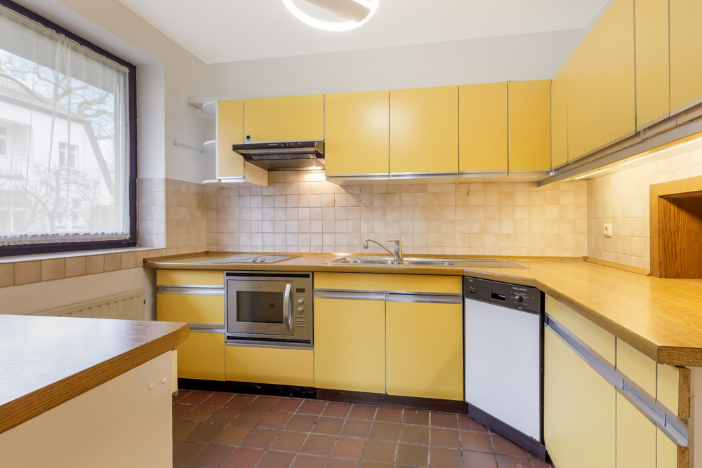 Küche mit gelben Schränken, Einbaugeräten, Spüle und großem Fenster.