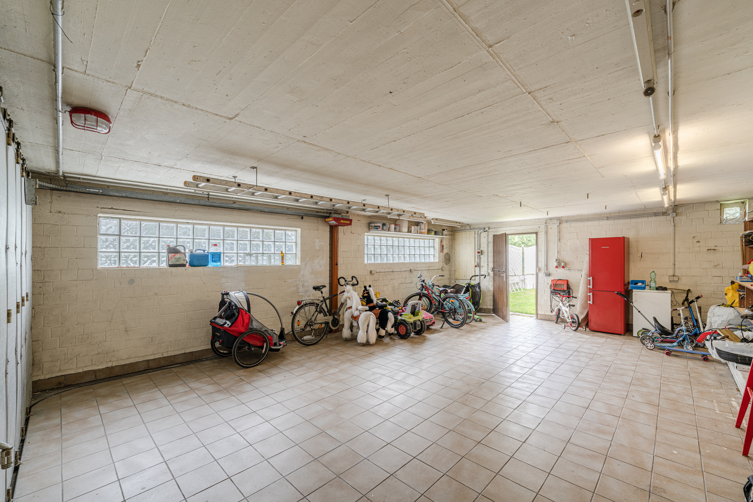 Große Garage mit mehreren Fahrrädern, Spielzeug, rotem Schrank und offenem Ausgang zum Garten.