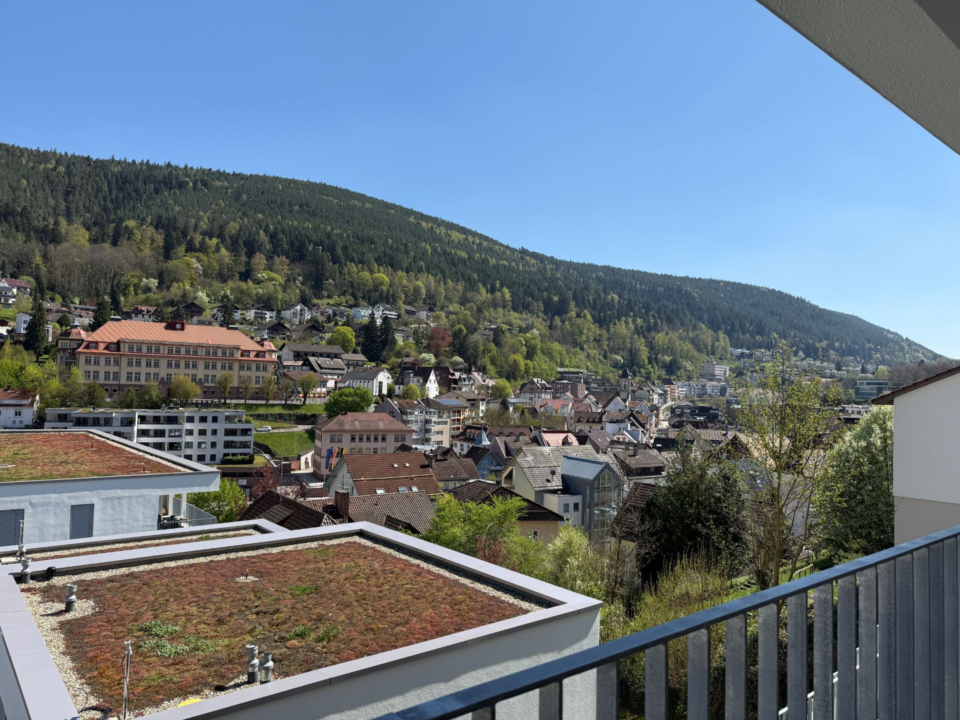 Blick von einem Balkon auf Dächer, Stadt und bewaldeten Hügel im Hintergrund.
