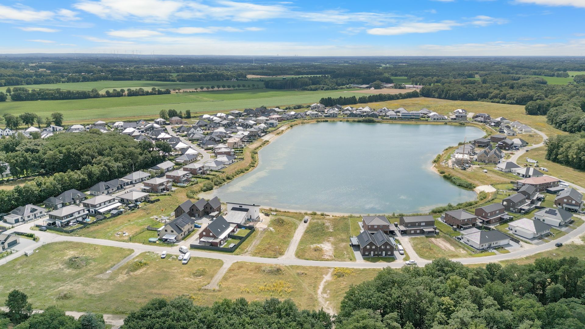 Luftaufnahme eines Wohngebiets mit Häusern um einen großen See und viel Grünfläche.