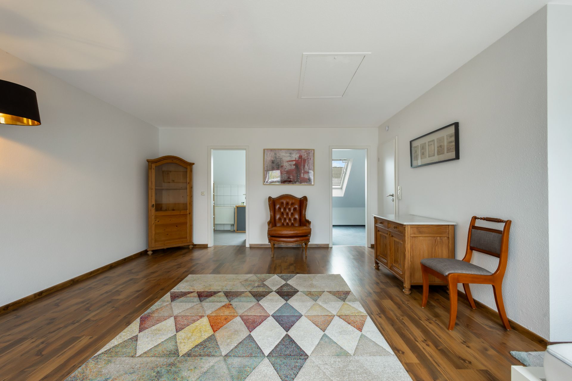 Wohnzimmer mit Parkettboden, Teppich, Holzschrank, Sessel und Sideboard, zwei Türen im Hintergrund.