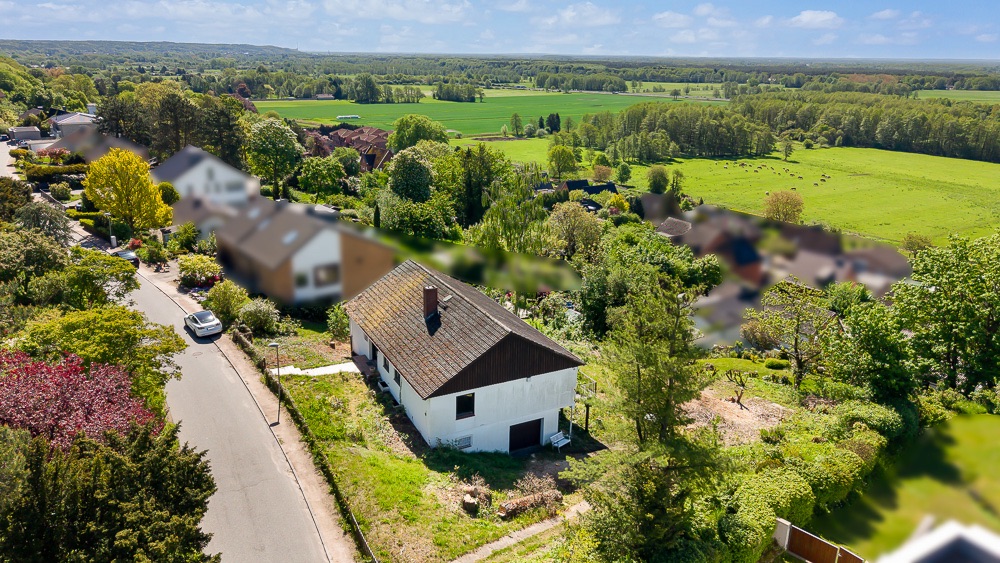 Weißes Einfamilienhaus mit Garten an einer ruhigen Straße, umgeben von viel Grün und Feldern.