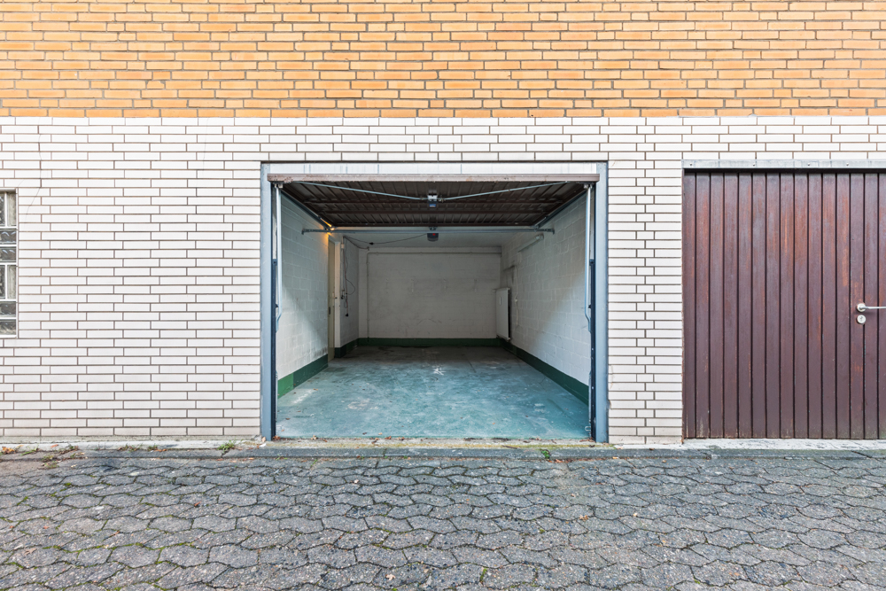 Offene Garage mit grünem Boden und weißen Wänden, daneben geschlossene Holztür.