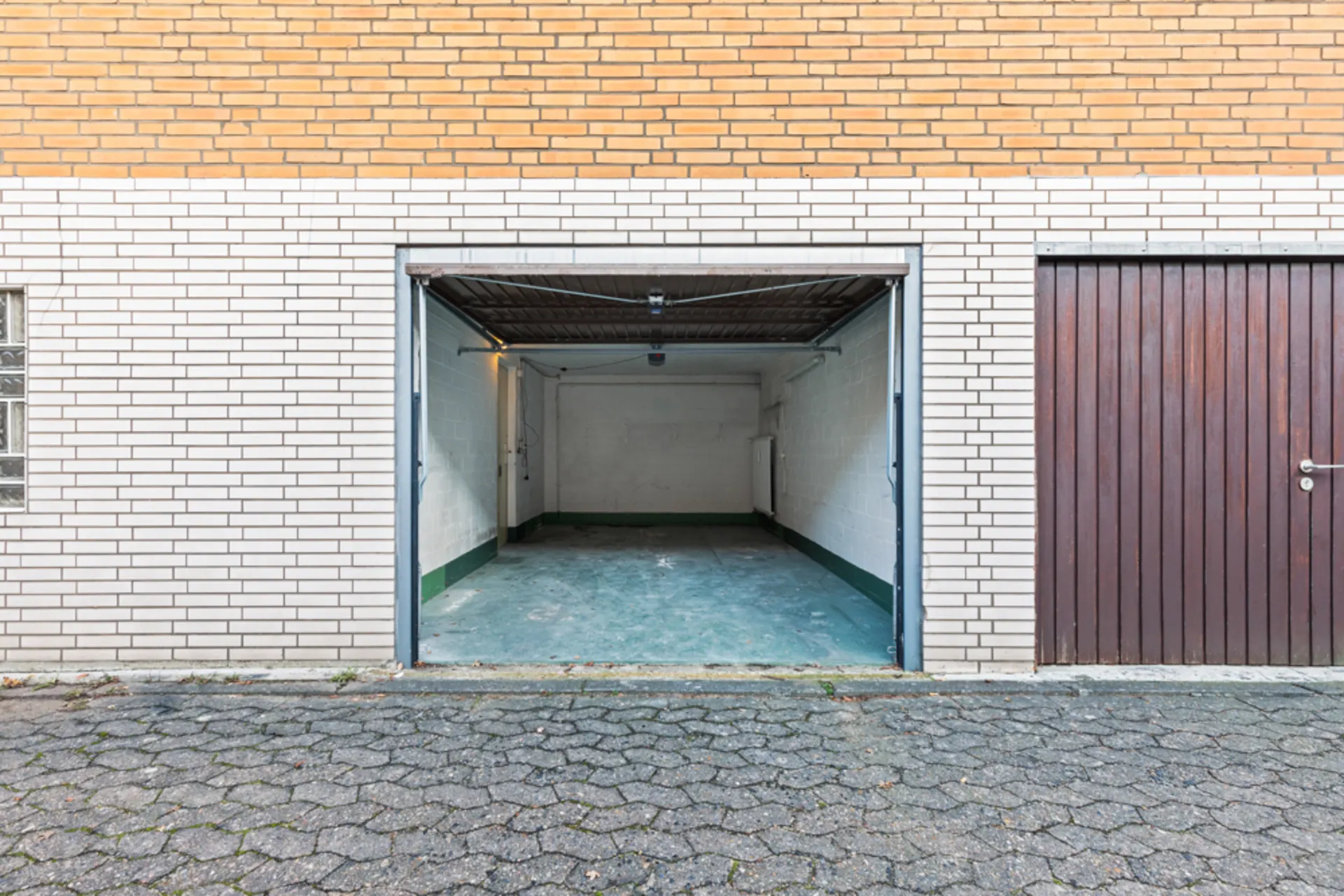 Offene Garage mit grünem Boden und weißen Wänden, daneben geschlossene Holztür.