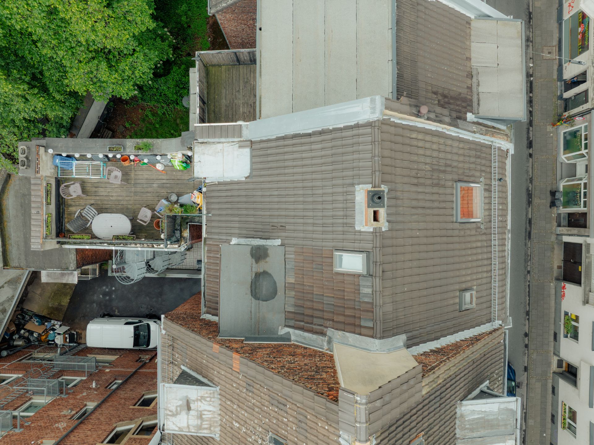 Draufsicht auf ein Gebäude mit Dachterrasse, Gartenmöbeln und Pflanzkübeln.