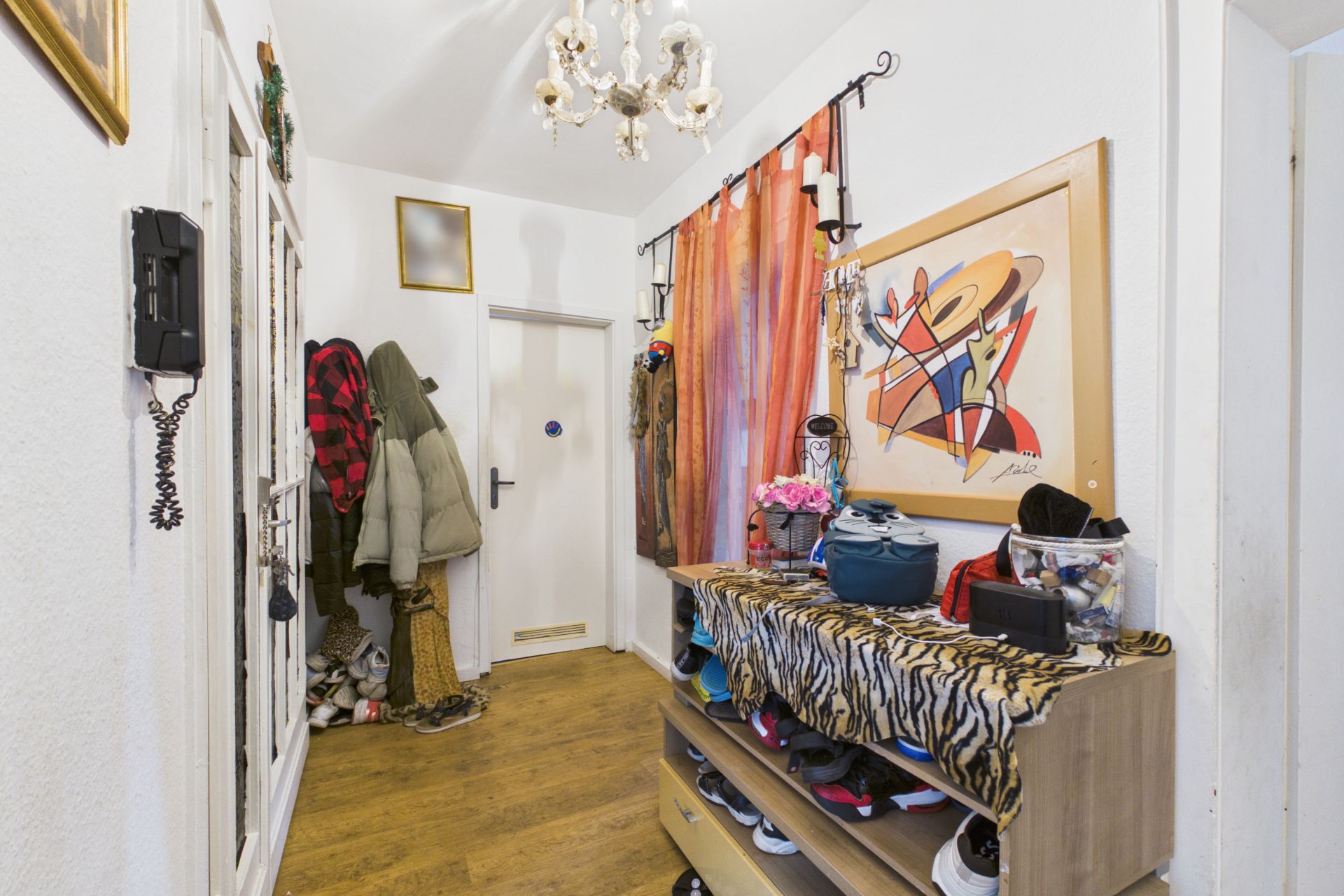 Flur mit Garderobe, Schuhregal, buntem Vorhang und modernem Wandbild.