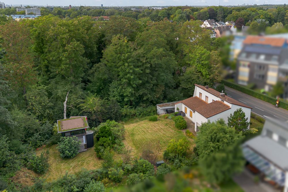 Luftaufnahme eines Wohnhauses mit großem Garten und Nebengebäude, umgeben von vielen Bäumen.