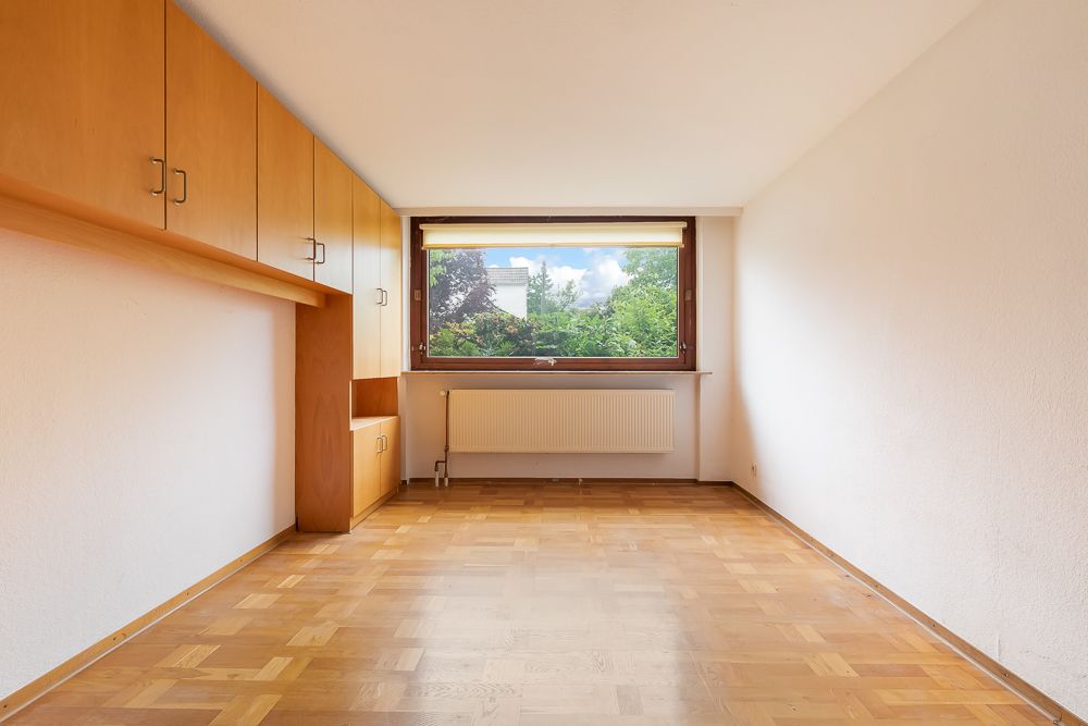 Leerer Raum mit Parkettboden, großen Einbauschränken und Fenster mit Blick ins Grüne.