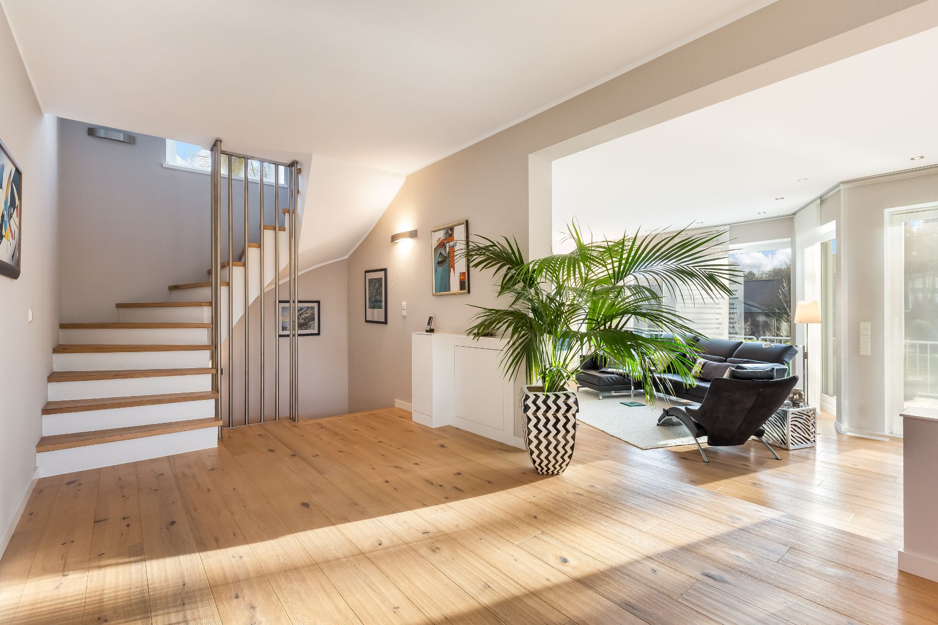 Heller Wohnbereich mit Holzfußboden, Treppe, großer Pflanze und modernen Möbeln.
