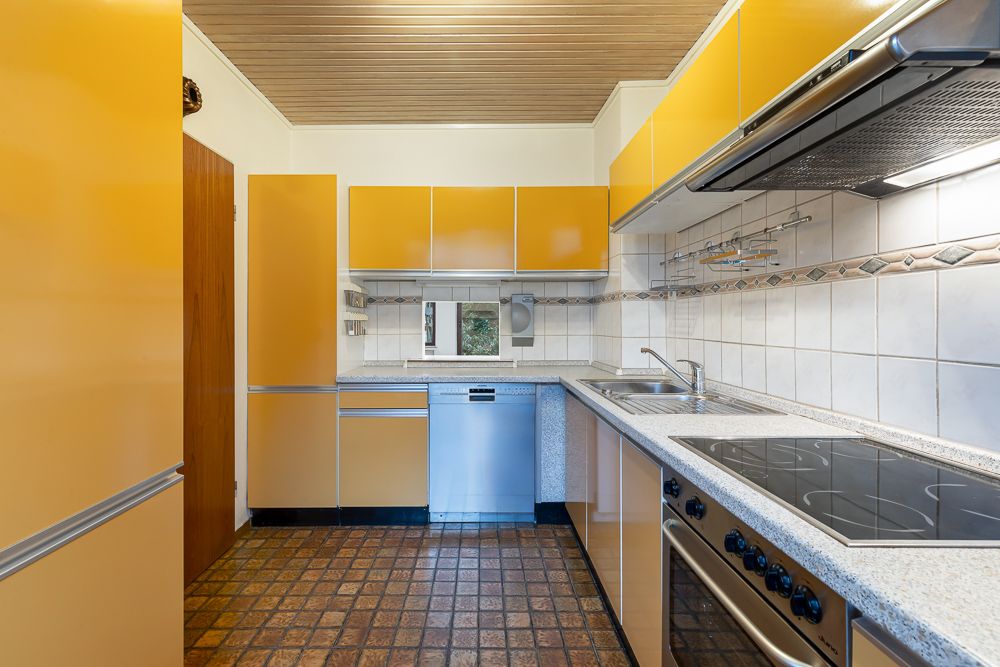 Küche mit gelben Schränken, Elektroherd, Spüle und Geschirrspüler, Fliesenboden und Holzdecke.