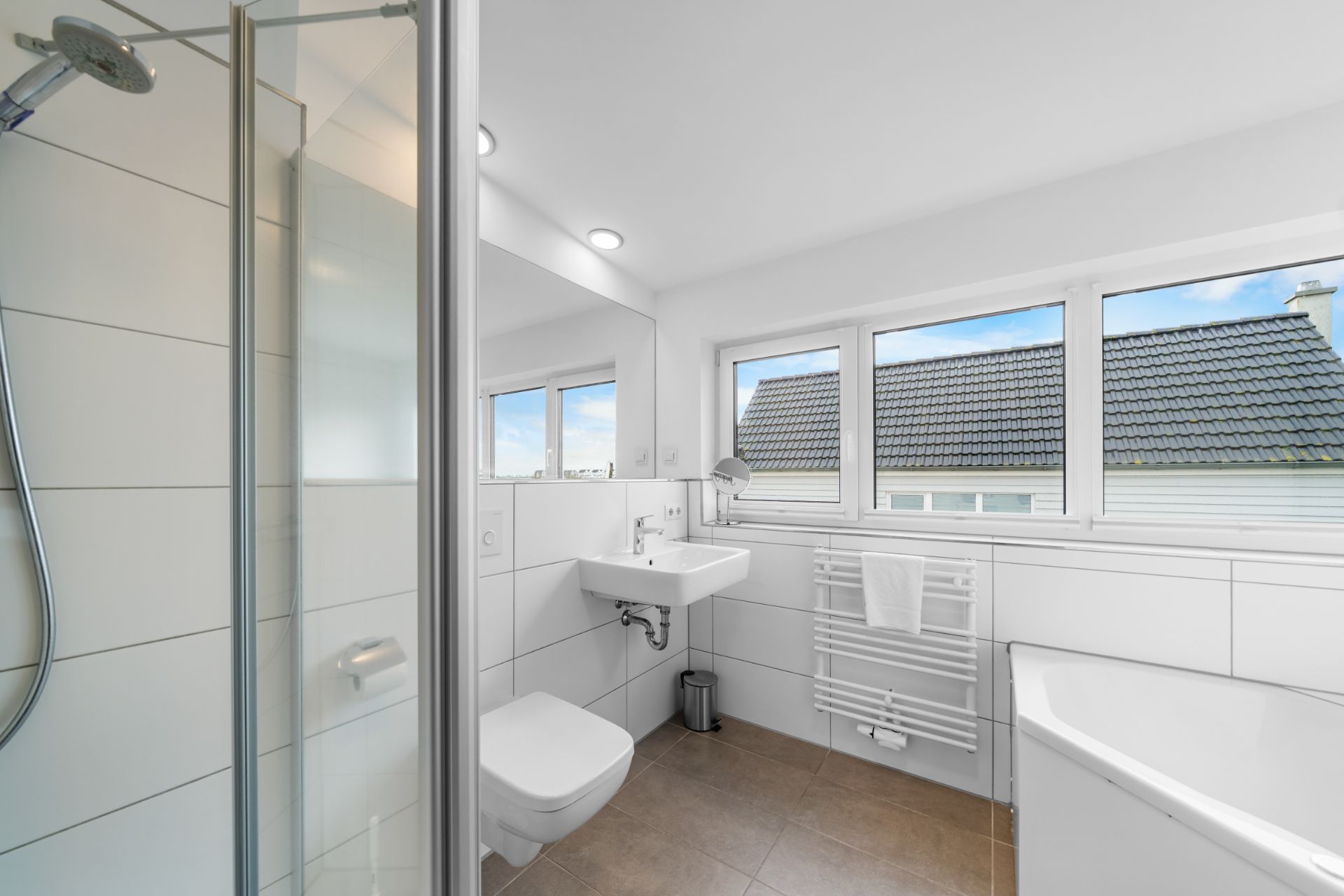 Modernes Badezimmer mit Dusche, Waschbecken, WC, Badewanne und großen Fenstern.