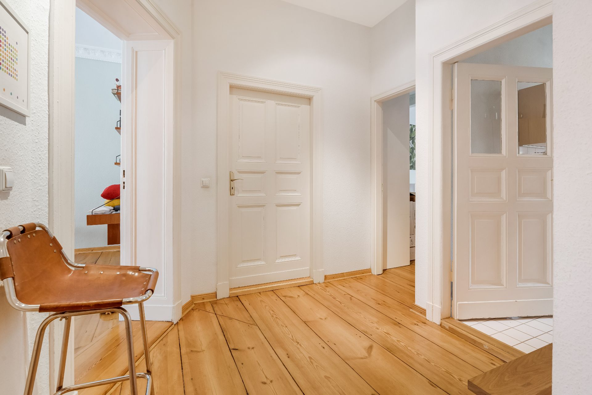 Heller Flur mit Holzboden, mehreren Türen und einem braunen Stuhl an der Wand.