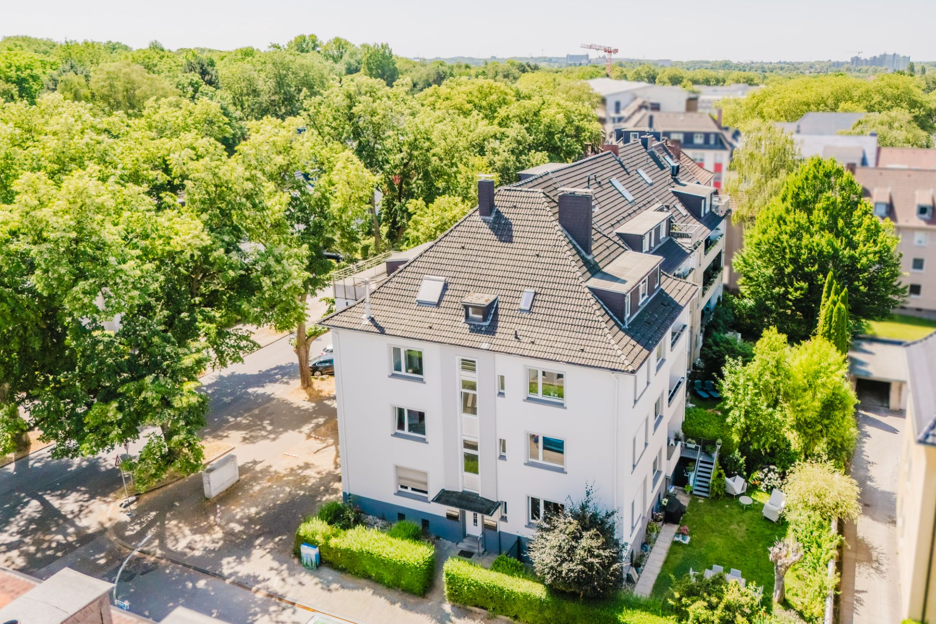 Mehrfamilienhaus mit Garten, umgeben von Bäumen und benachbarten Wohnhäusern.