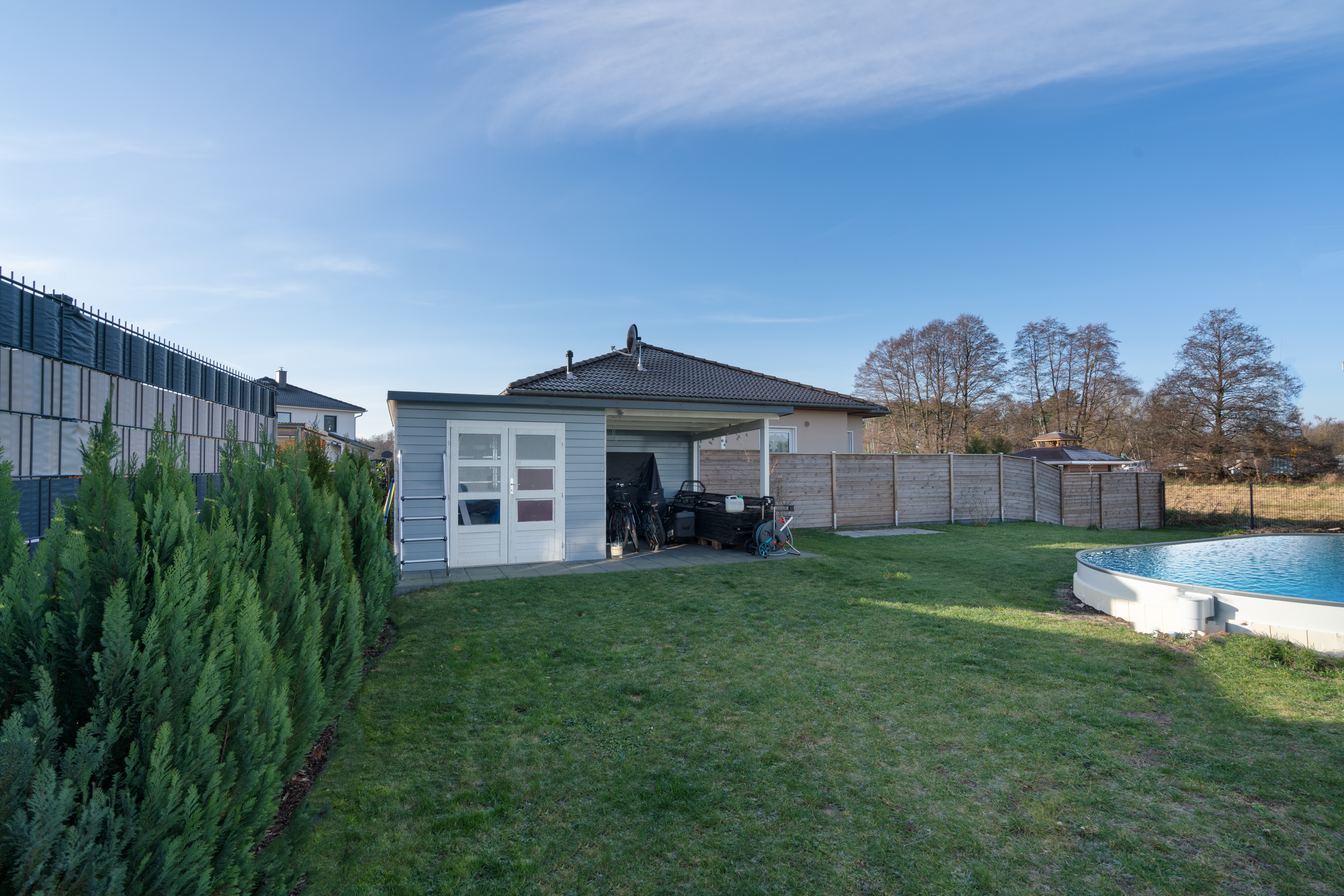 Garten mit Rasen, Gartenhaus, überdachtem Bereich und rundem Pool.