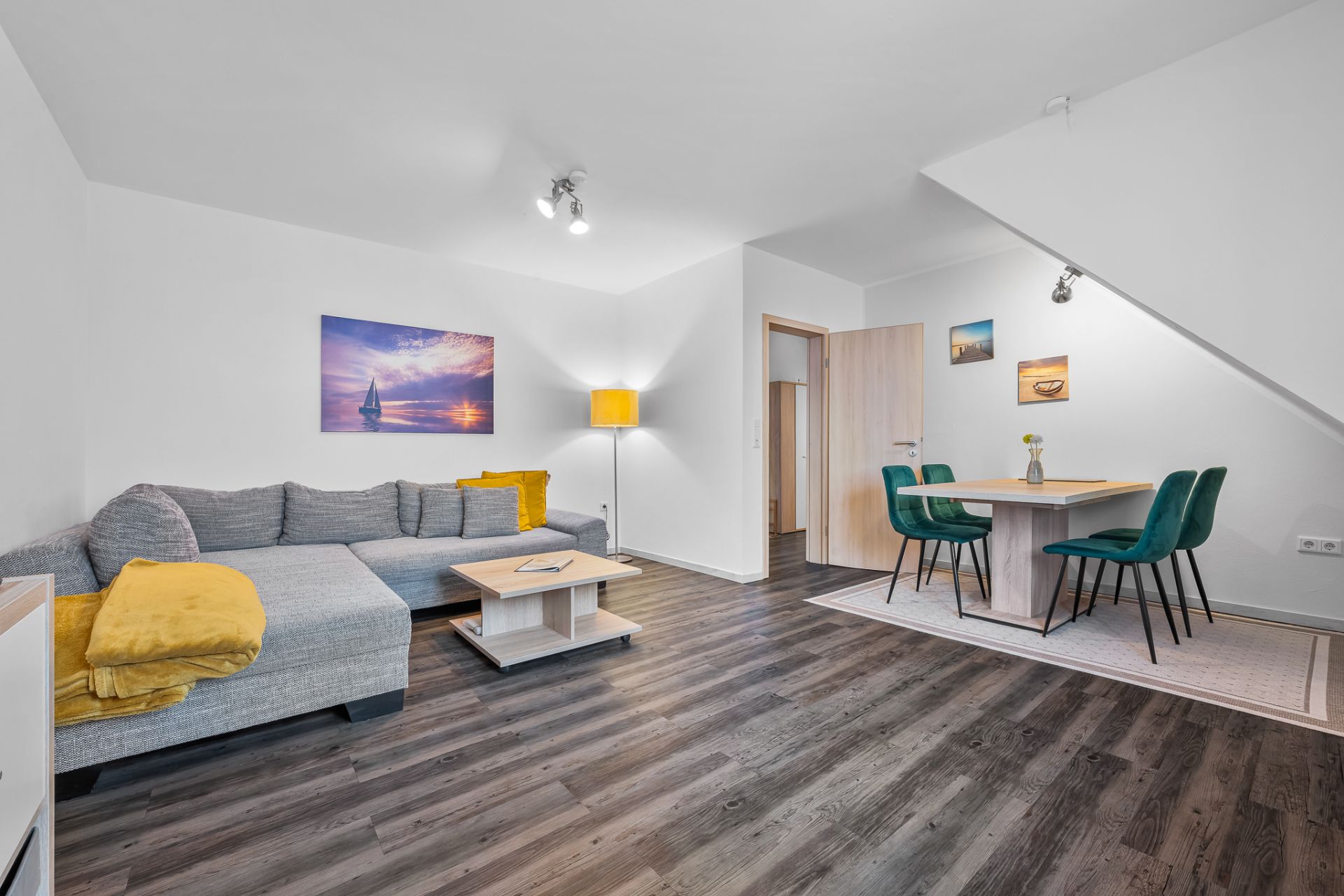 Modernes Wohnzimmer mit grauem Sofa, Couchtisch, Stehlampe und Essbereich mit grünen Stühlen.