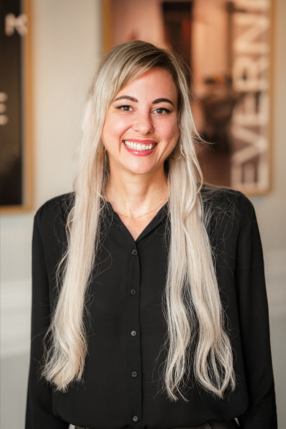 Frau mit langen, blonden Haaren und schwarzer Bluse lächelt in die Kamera.