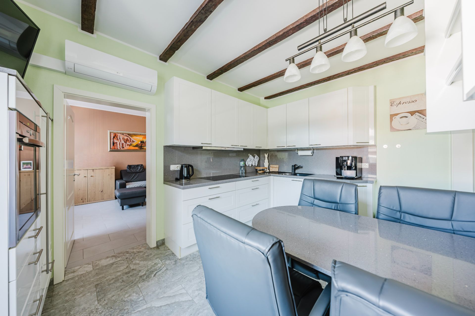 Moderne Küche mit weißen Schränken, Esstisch und blauen Stühlen, Sicht auf angrenzendes Wohnzimmer.