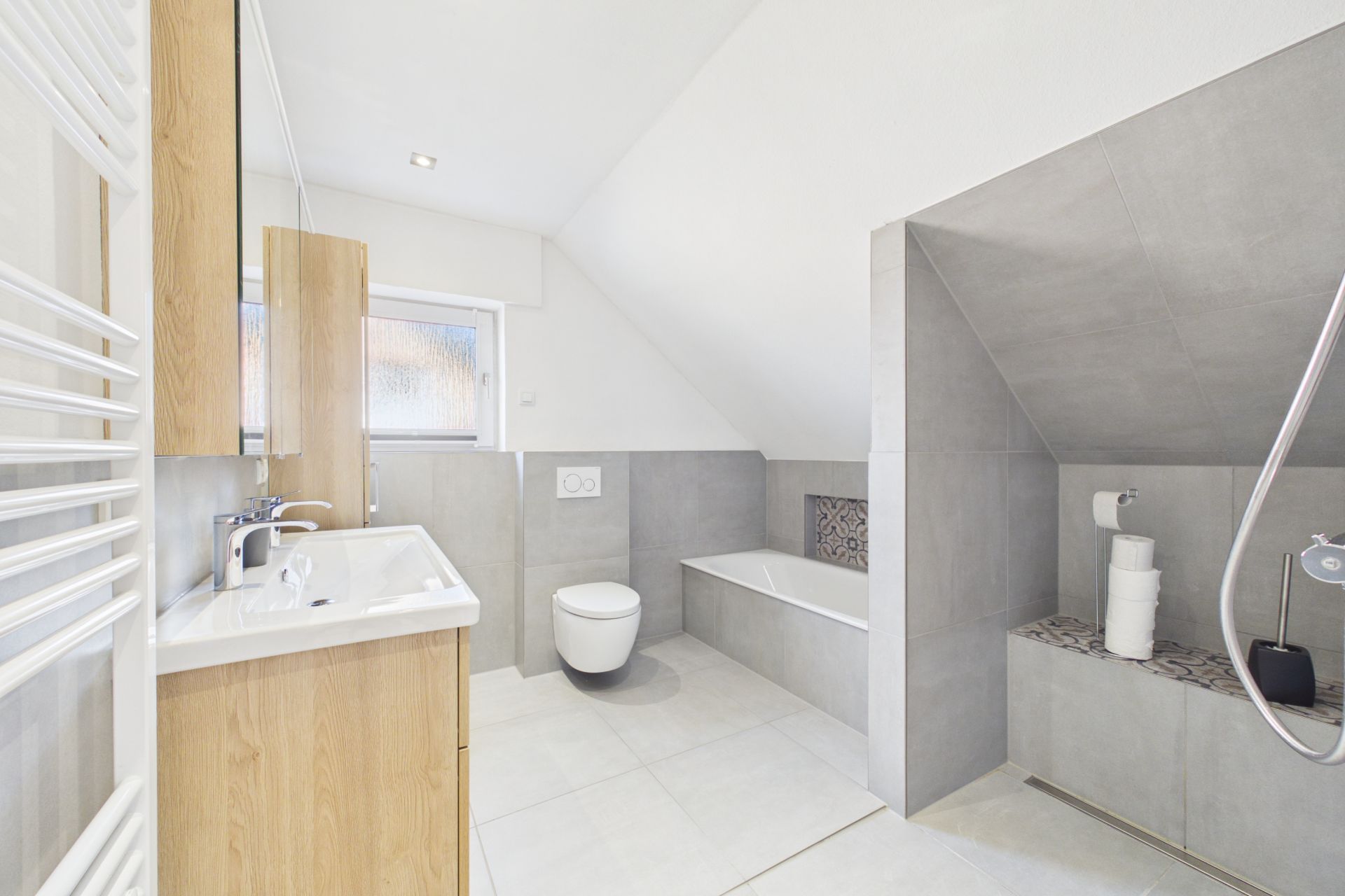 Modernes Badezimmer mit Badewanne, WC, Waschbecken und großem Spiegel unter Dachschräge.
