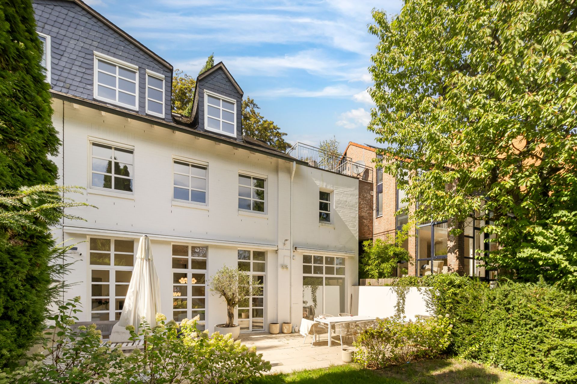 Helles, modernes Wohnhaus mit Garten, Terrasse und großen Fenstern, umgeben von Bäumen.