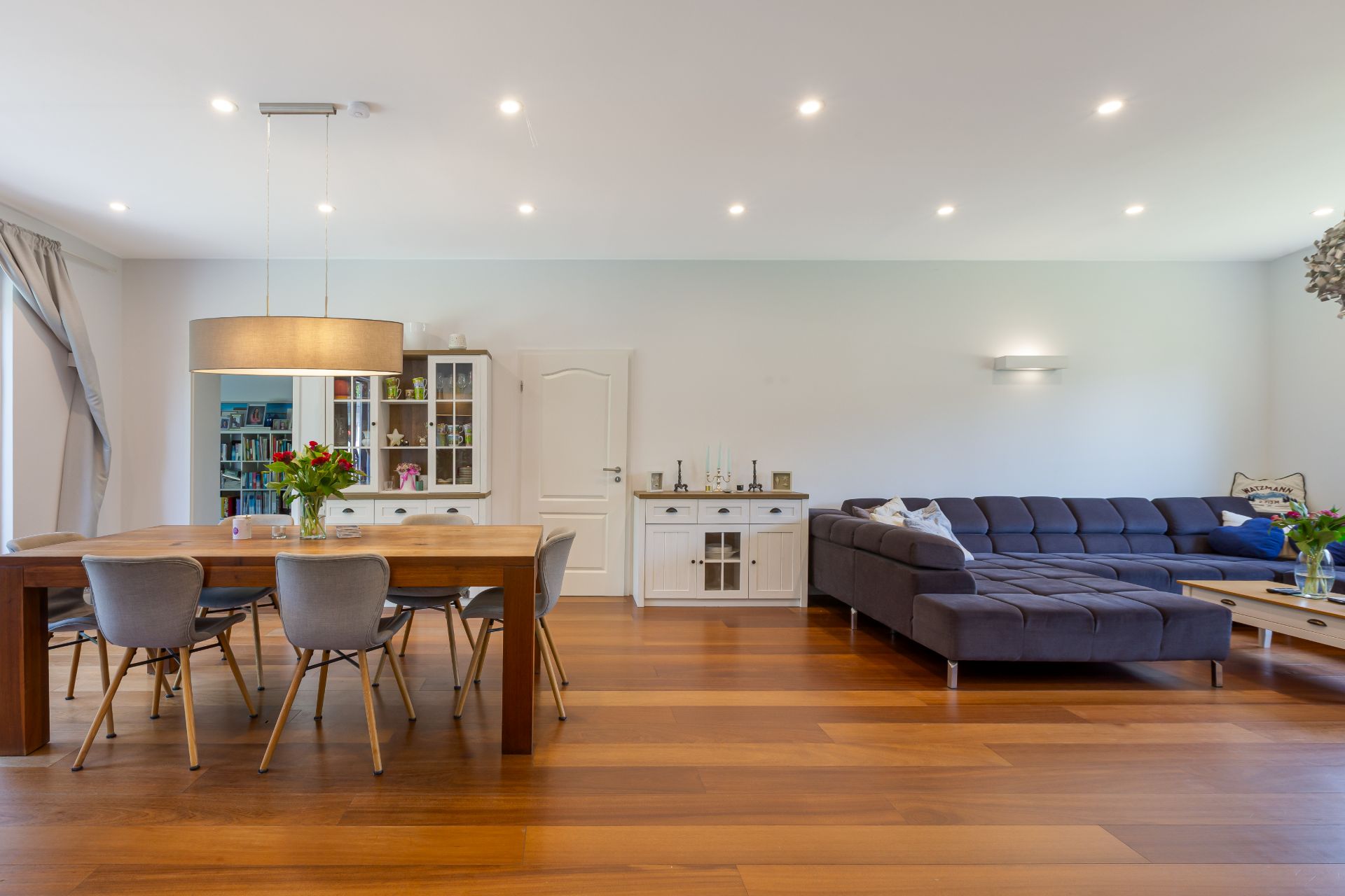 Modernes Wohnzimmer mit Holzboden, grauem Sofa und Essbereich mit Holztisch und Stühlen.