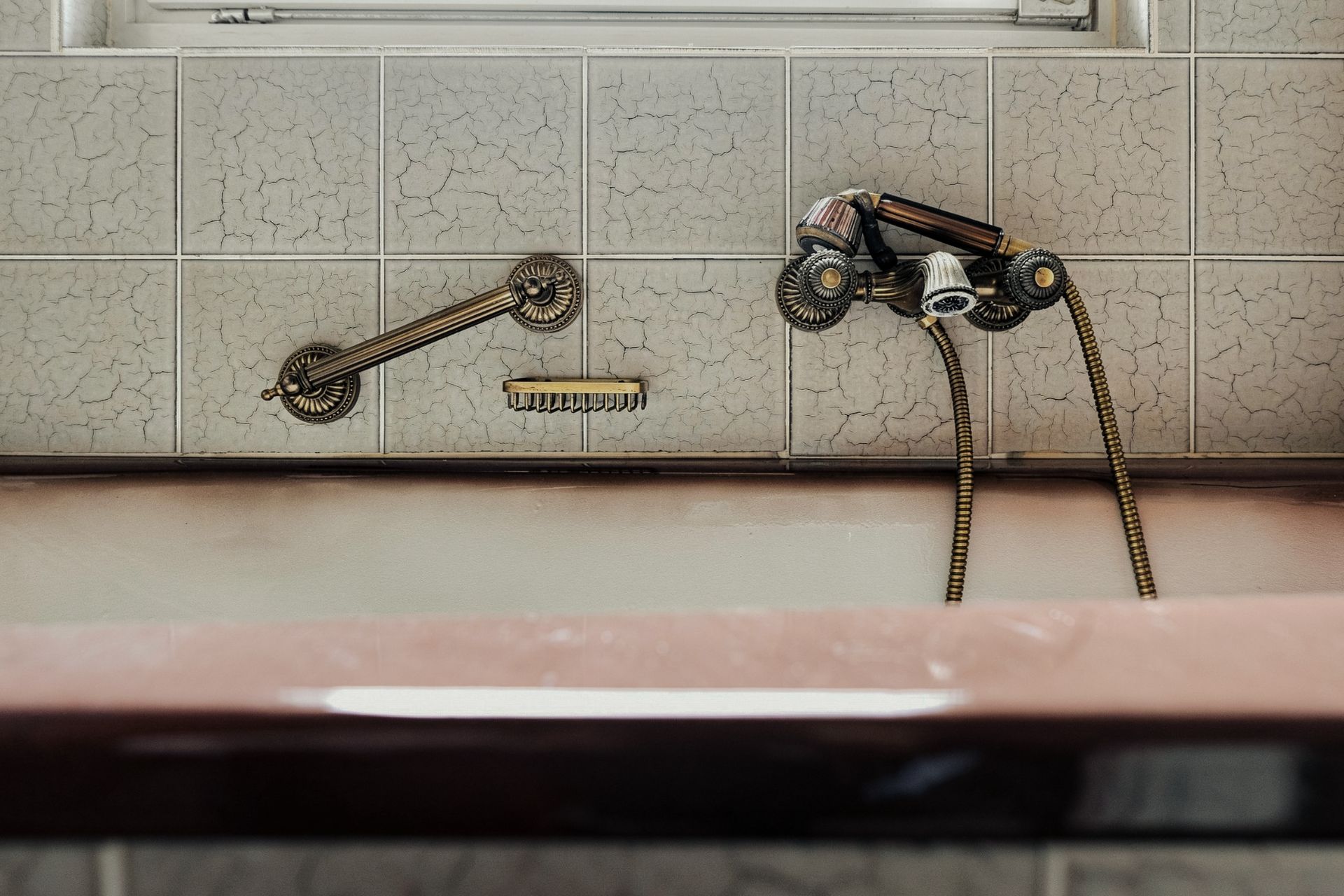 Alte Badewanne mit Messingarmaturen und gemusterten Fliesen an der Wand.