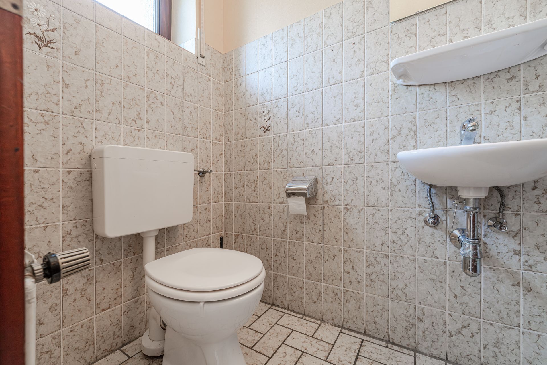 Kleines Badezimmer mit Toilette, Waschbecken, Toilettenpapier und gefliesten Wänden.