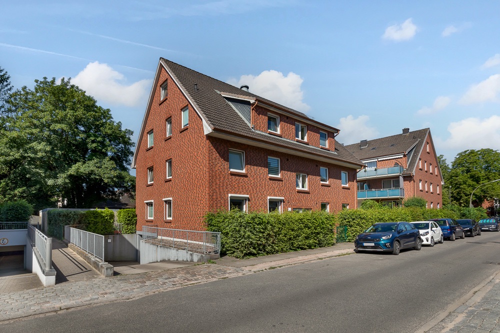 Rotes Mehrfamilienhaus mit Satteldach an einer ruhigen Straße mit geparkten Autos.
