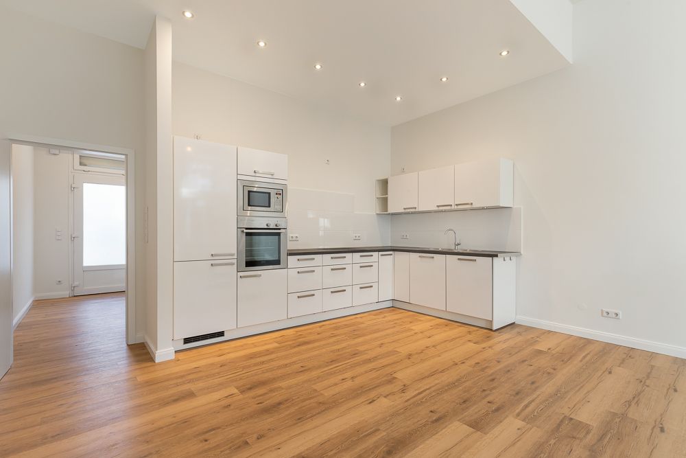 Helle Einbauküche mit weißen Schränken und Holzfußboden in offenem Wohnraum.