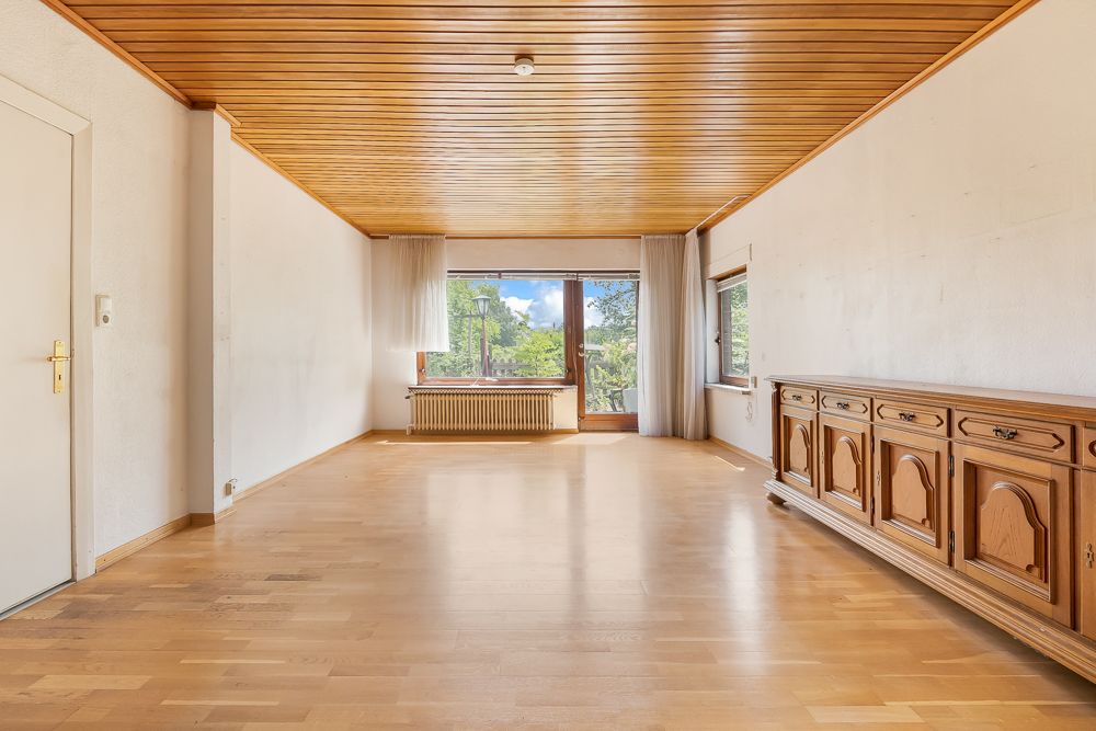 Helles Wohnzimmer mit Holzdecke, Parkettboden, Sideboard, Fenster und Glastür zum Garten.