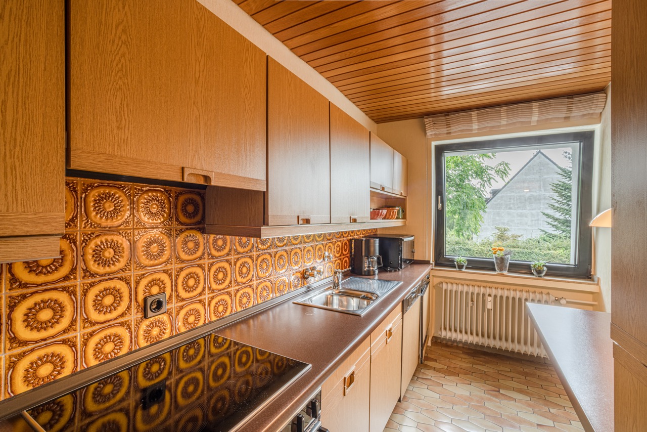 Küche mit Holzmöbeln, gemusterter Fliesenwand und großem Fenster mit Blick nach draußen.