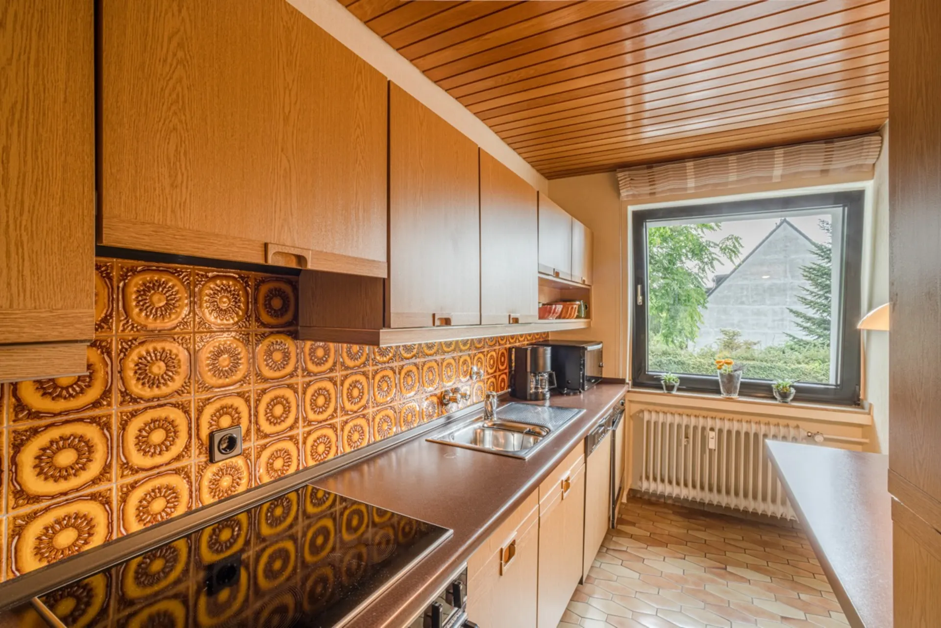 Küche mit Holzmöbeln, gemusterter Fliesenwand und großem Fenster mit Blick nach draußen.