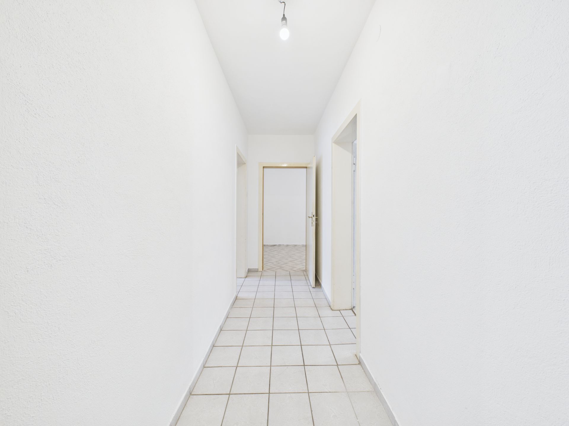 Heller Flur mit weißen Wänden, Fliesenboden und mehreren Türöffnungen in einer Wohnung.