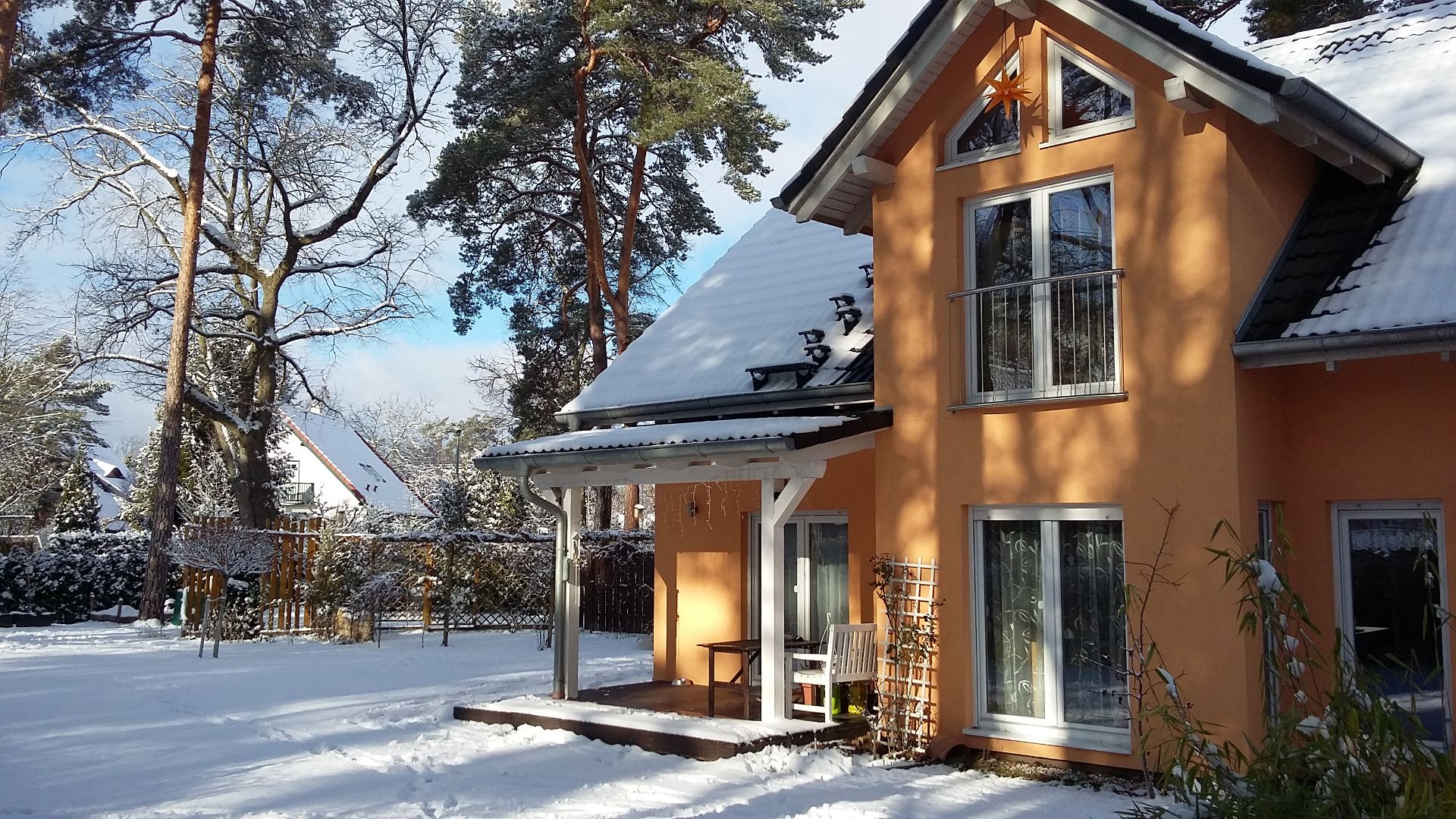 Modernes Einfamilienhaus mit orangefarbener Fassade im verschneiten Garten.