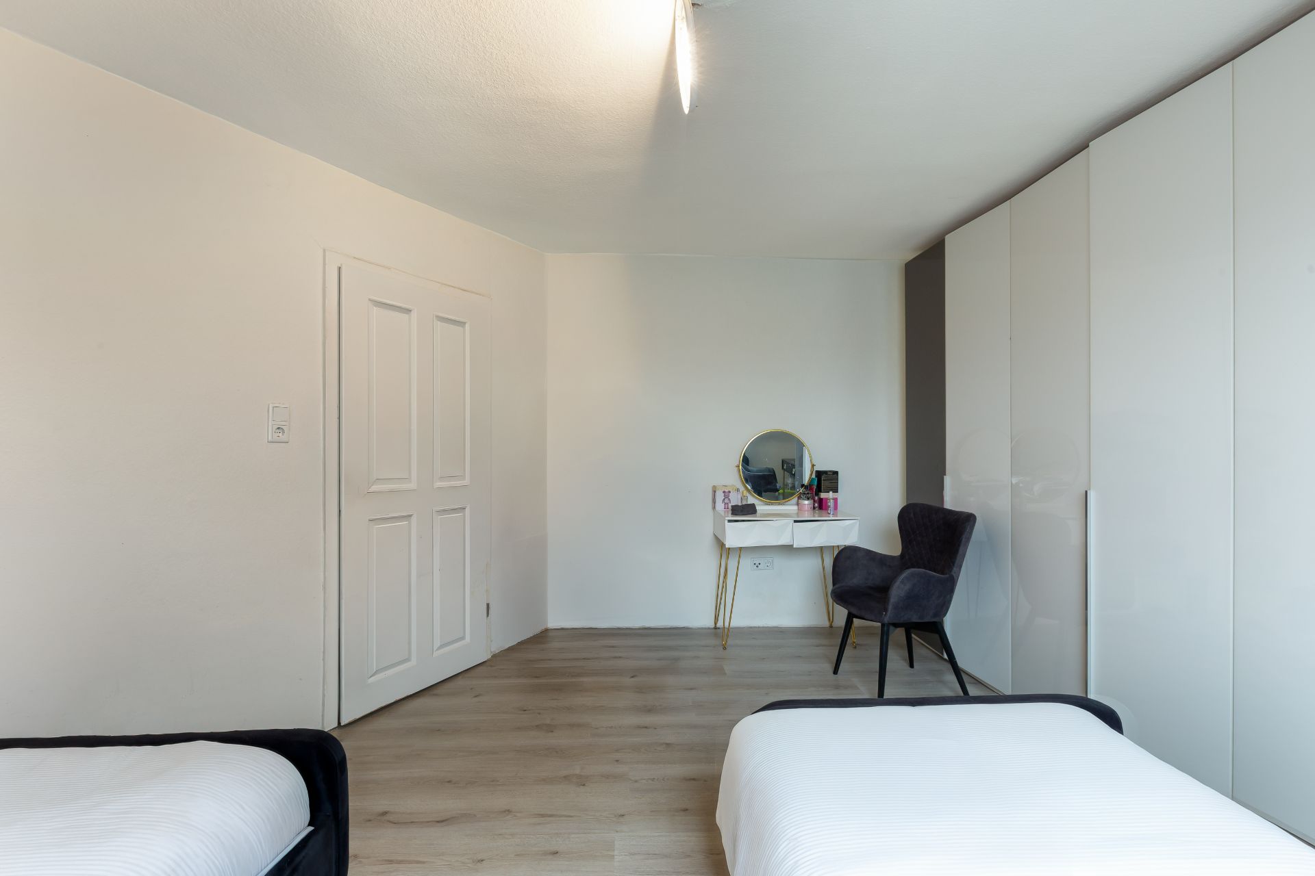Schlafzimmer mit zwei Betten, einem Schminktisch mit Spiegel, Stuhl und großem weißen Kleiderschrank.