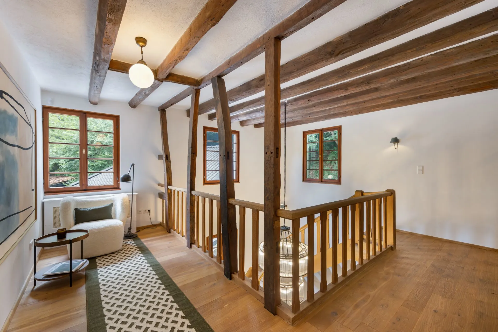 Flur mit sichtbaren Holzbalken, Sessel, Teppich und Fenster mit Holzrahmen.