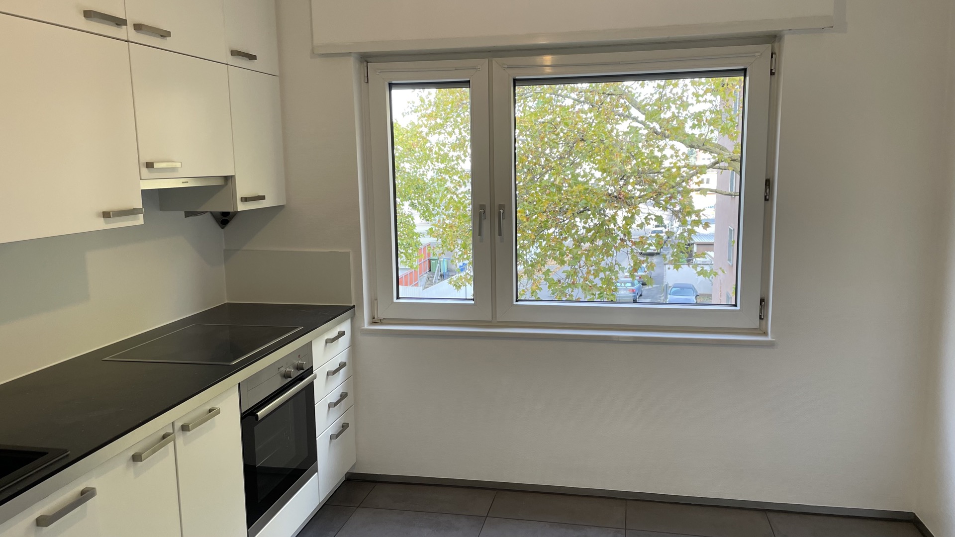 Helle Küche mit weißen Schränken, Herd und großem Fenster mit Blick auf Bäume.