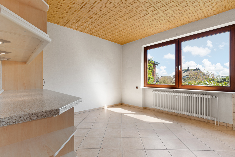 Heller Raum mit Fliesenboden, großem Fenster und Holzdecke, Heizung unter dem Fenster.