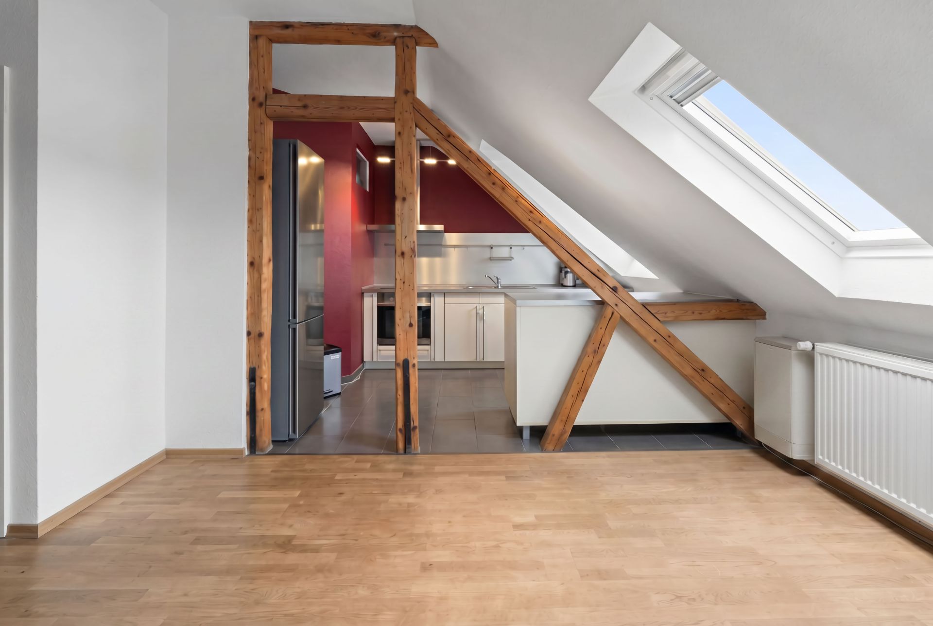 Offener Wohnraum mit Holzbalken, Dachfenster und moderner Einbauküche im Hintergrund.
