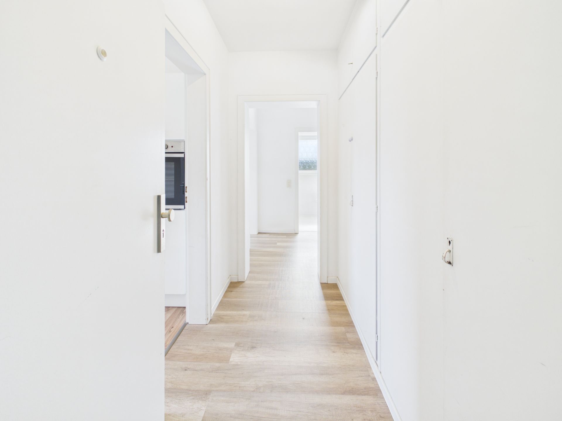 Heller Flur mit Holzfußboden und weißen Wänden, Türen führen in weitere Räume.