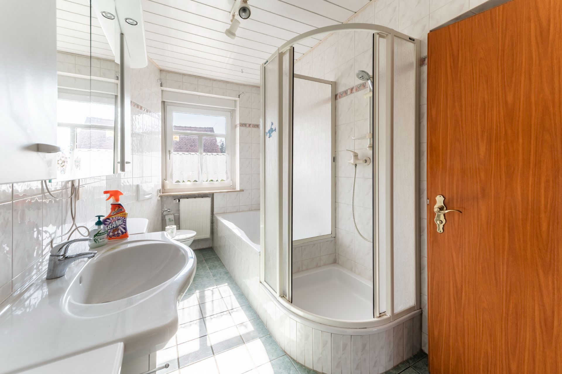 Helles Badezimmer mit Dusche, Badewanne, Waschbecken, Fenster und Holztür.