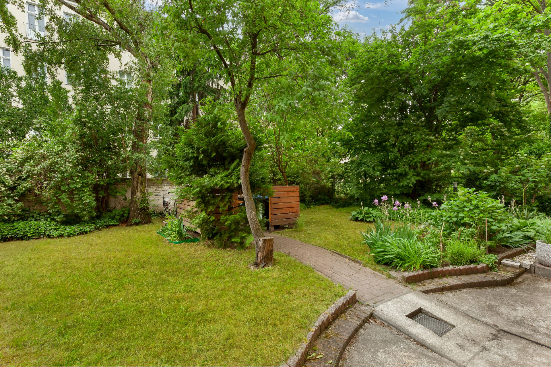 Grüner Garten mit Bäumen, Rasenfläche, Blumenbeeten und kleinem Weg.