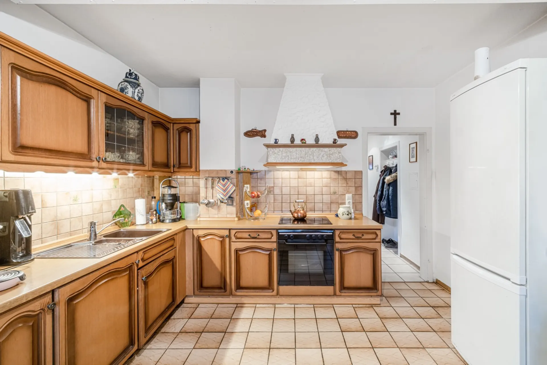 Küche mit Holzschränken, Herd, Spüle und weißem Kühlschrank auf gefliestem Boden.