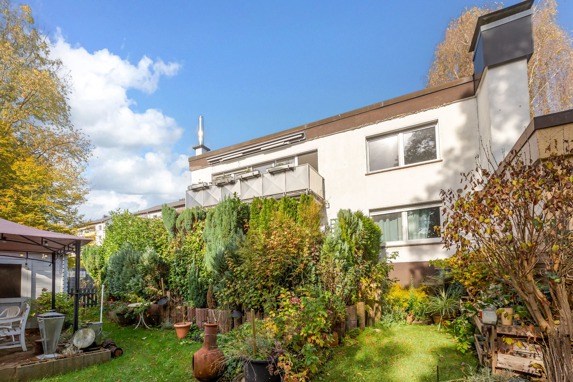Zweistöckiges Wohnhaus mit Balkon und begrünter Garten mit Pavillon im Vordergrund.