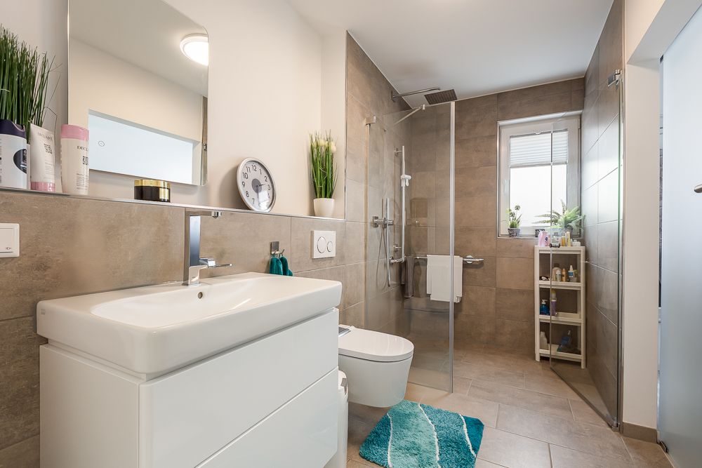 Modernes Badezimmer mit Waschbecken, Toilette, Dusche und Fenster, Pflanzen auf Regal und Fensterbank.