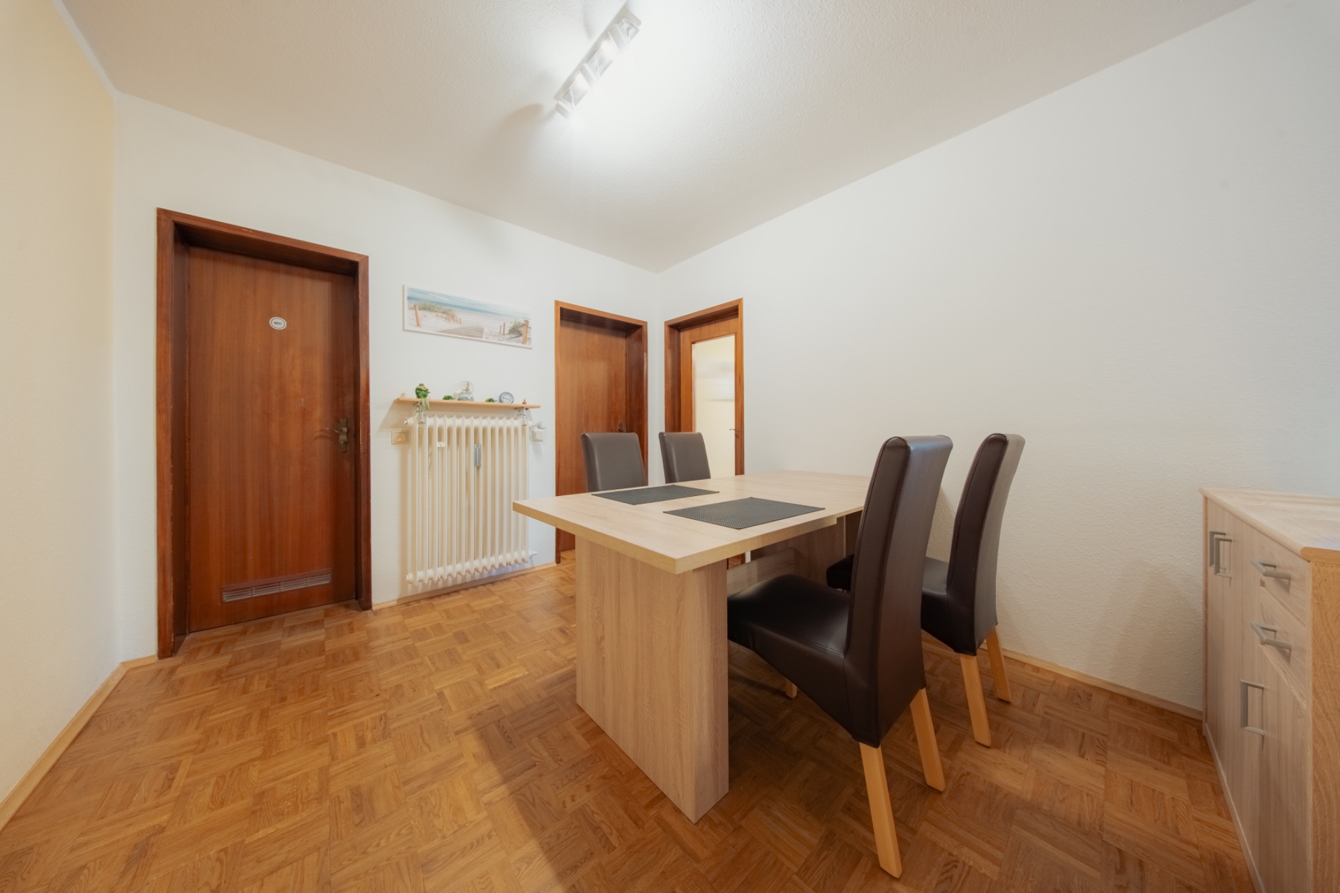 Esszimmer mit Holztisch, vier Stühlen und Türen, Parkettboden und weißer Wand.