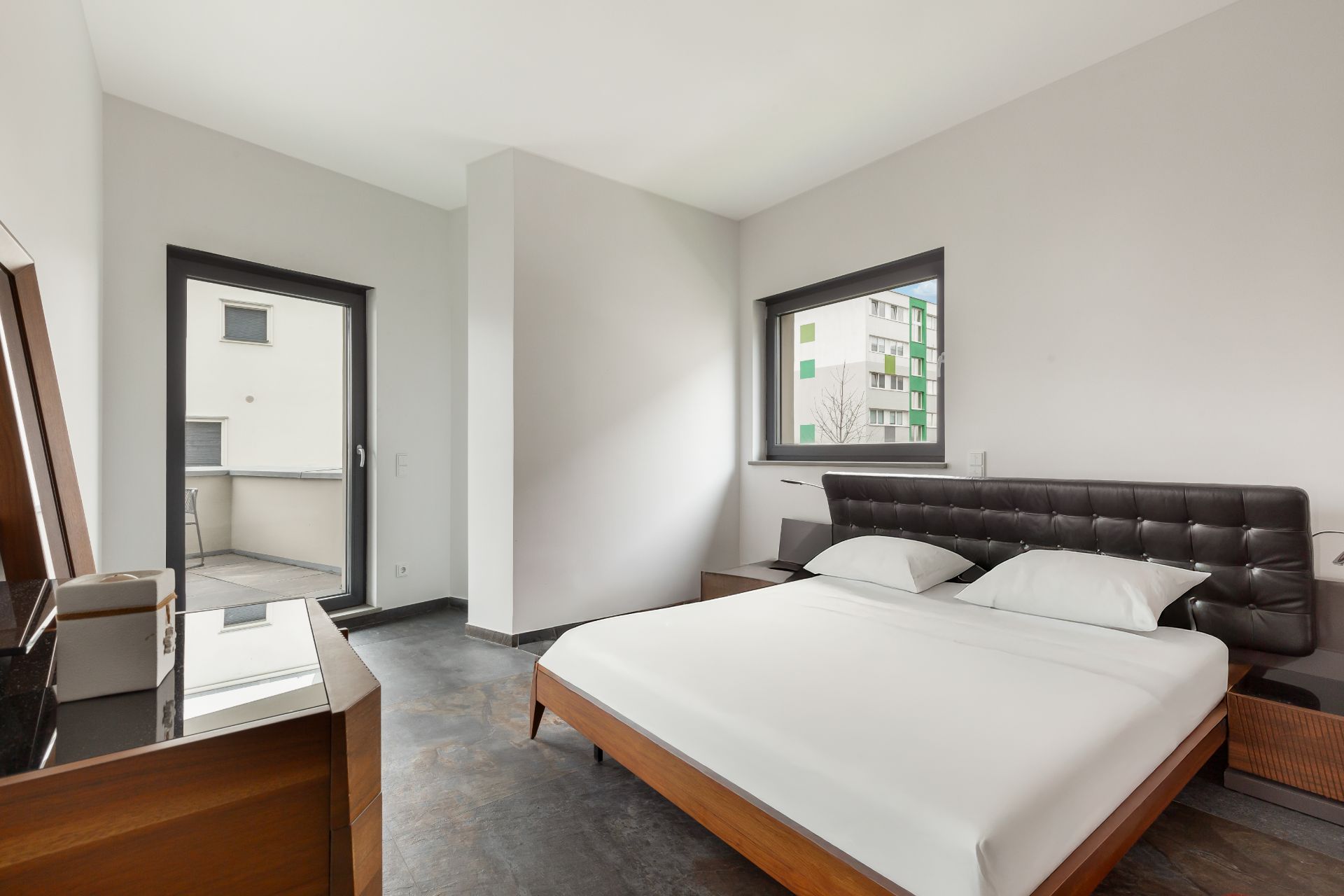 Modernes Schlafzimmer mit Doppelbett, Nachttischen und Zugang zu einem Balkon.