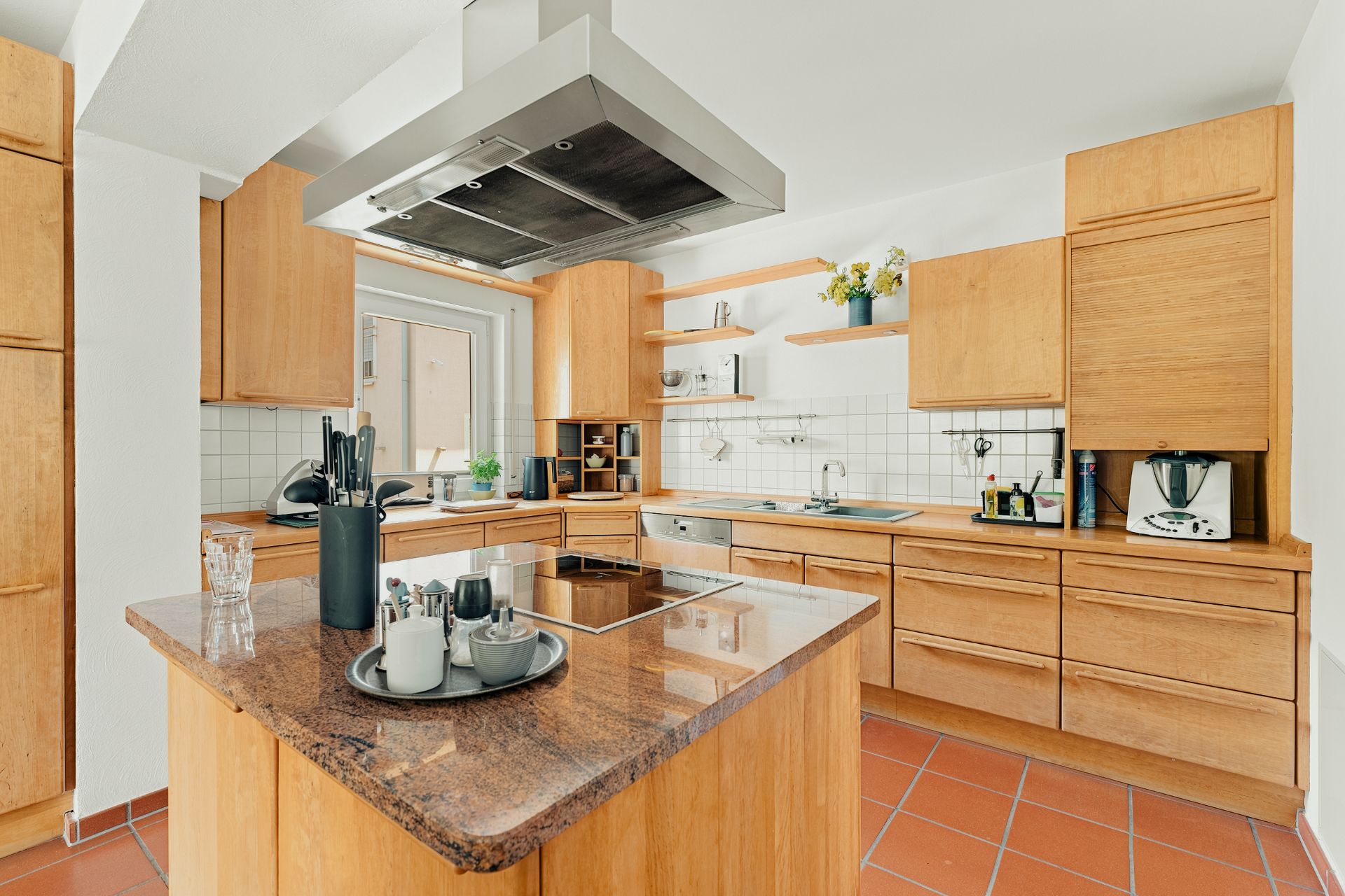 Moderne Küche mit Kochinsel, Holzmöbeln, offenem Regal und großen Fenstern.